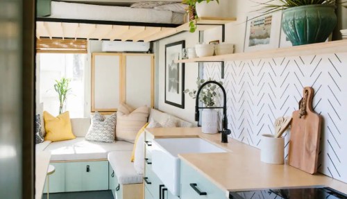 Cozy tiny home interior with a kitchen, seating area, and lofted bed, featuring modern decor and natural light.