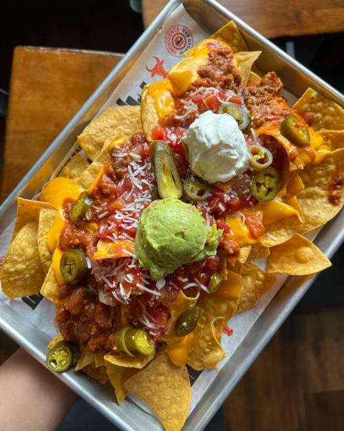 A tray of nachos topped with cheese, chili, jalapeños, guacamole, sour cream, and salsa.