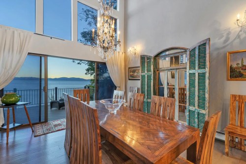A spacious dining room with a wooden table, chairs, and large windows showcasing a scenic view of the lake.
