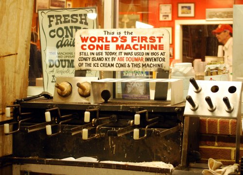Sign about the world's first cone machine, used since 1905, displayed in an ice cream shop with vintage decor.