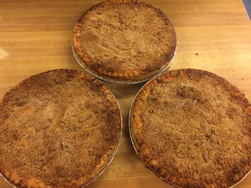 Three freshly baked pies with crumbly tops, resting on a wooden surface.