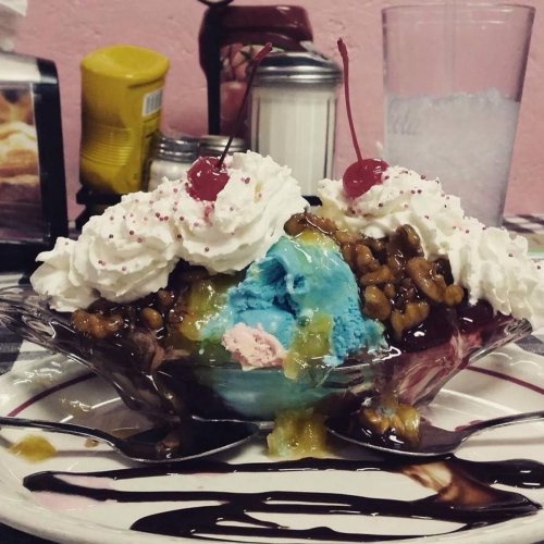 A colorful ice cream sundae with whipped cream, cherries, chocolate syrup, and toppings in a glass dish.