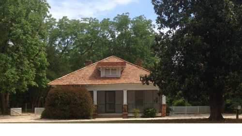 A charming house with a sloped roof, surrounded by trees and greenery, featuring a porch and stone accents.