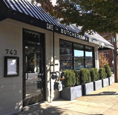 Exterior of Butchertown Grocery, featuring a cafe entrance, large windows, and neatly trimmed shrubs.