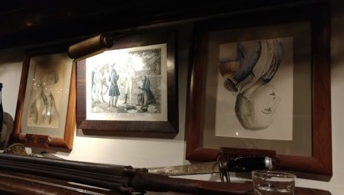Framed historical illustrations and artifacts displayed on a wall, including a rifle and decorative plaques.