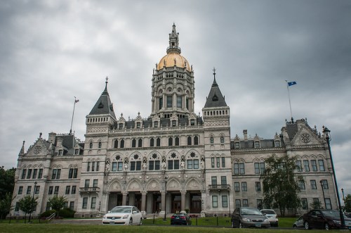 The Connecticut State Capitol building features a golden dome and intricate architectural details under a cloudy sky.