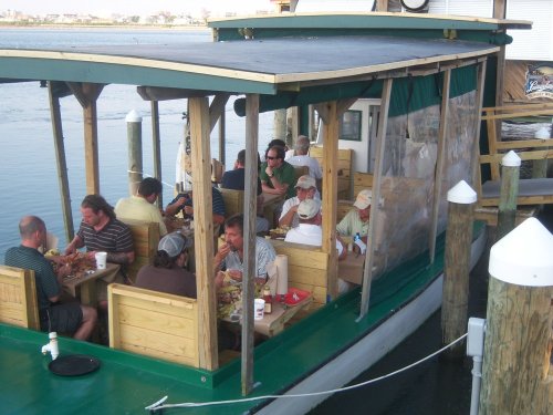 A group of people dining on a boat with wooden seating, enjoying a meal by the water on a sunny day.