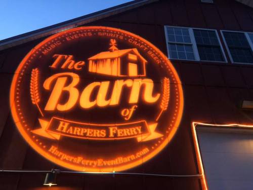 A lit sign on a barn wall reads "The Barn of Harpers Ferry," promoting music, events, spirits, and craft beer.