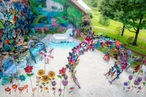 A colorful garden with vibrant flowers, a unicorn statue, and artistic decorations against a lush green backdrop.