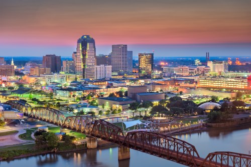 A vibrant city skyline at dusk, featuring illuminated buildings and a bridge over a river.