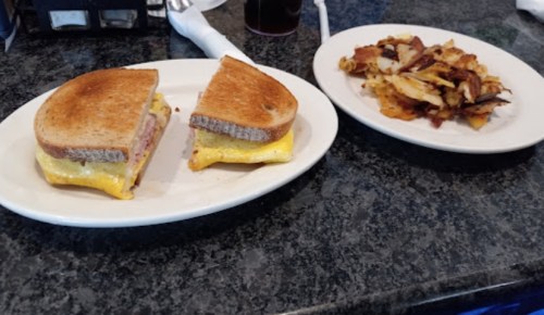 A toasted sandwich with cheese and ham, alongside a plate of crispy hash browns.