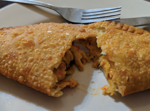 A golden, flaky pastry filled with colorful vegetables, partially cut open on a white plate with a fork and knife.