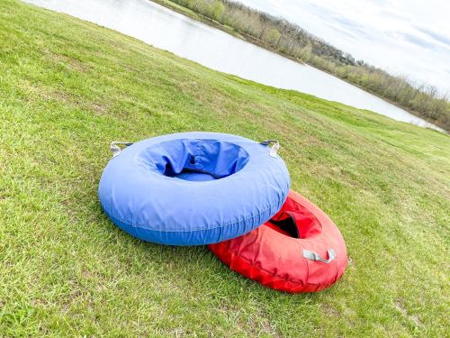 Two inflatable tubes, one blue and one red, resting on green grass near a calm body of water.