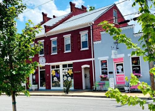 A charming red and gray building with flower decorations, storefronts, and trees lining the street under a blue sky.