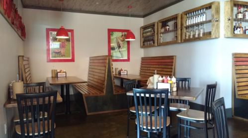 Cozy restaurant interior with wooden booths, tables, and red pendant lights, featuring framed artwork on the walls.