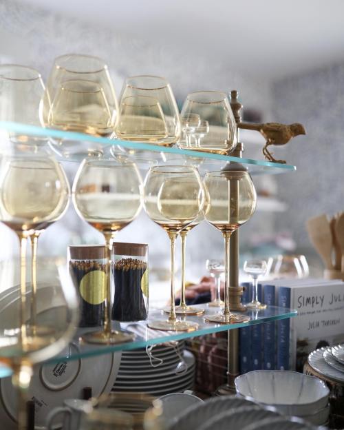 A shelf displaying elegant glassware, including wine glasses and decorative items, with a small bird figurine perched on top.