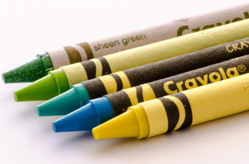 Four Crayola crayons in green, teal, blue, and yellow arranged on a white background.