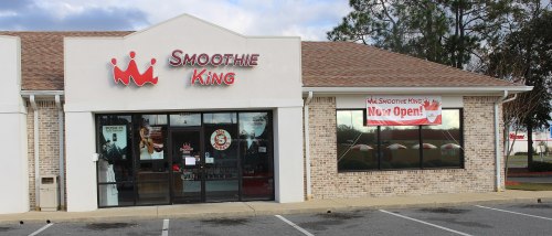 Exterior of a Smoothie King store with a "Now Open!" banner and large windows.