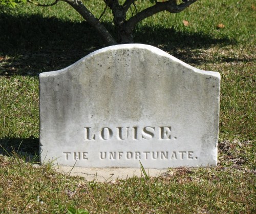 A weathered gravestone reads "LOUISE. THE UNFORTUNATE." set in a grassy area with a tree in the background.