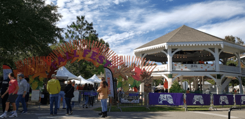 Colorful archway reading "Fall Fest" with a gazebo in the background and people enjoying the event.