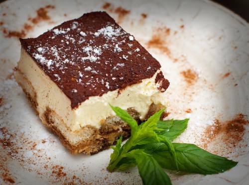 A slice of tiramisu on a decorative plate, garnished with mint leaves and a dusting of cocoa powder.