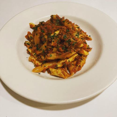 A plate of pasta with a rich tomato sauce, garnished with herbs, served on a white dish.