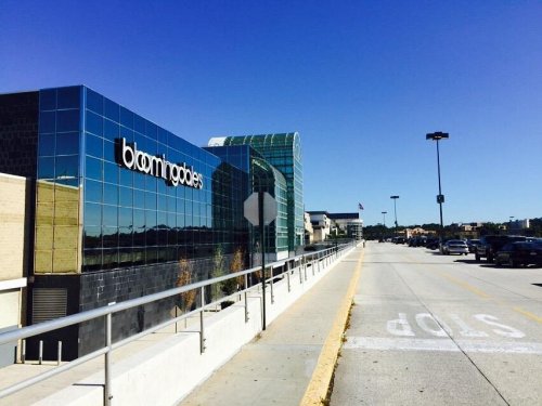 A modern building with reflective glass, featuring the sign "bloomingdales," alongside a clear blue sky and empty parking lot.