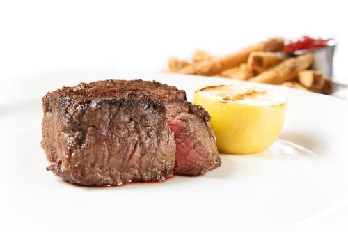 A perfectly cooked steak with a slice of grilled lemon, served alongside crispy fries on a white plate.