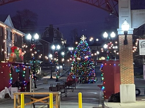 A festive scene featuring a decorated Christmas tree surrounded by colorful lights and holiday decorations at night.