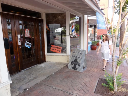 A woman walks past a salon with an "Open" sign and a decorative bear sign outside on a brick sidewalk.