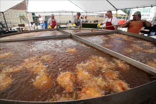 A large outdoor frying setup with several people cooking food in bubbling oil under a tent.
