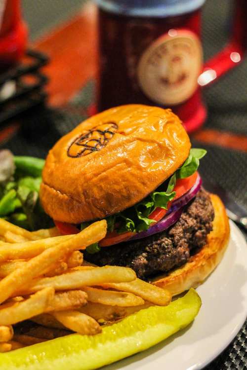 A juicy burger with lettuce, tomato, and onion, served with fries and a pickle on a white plate.