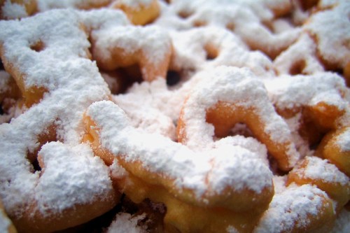 Close-up of powdered sugar-dusted funnel cakes, showcasing their crispy texture and intricate shapes.