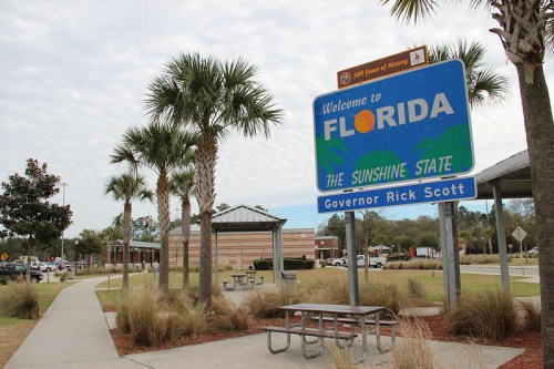 Welcome sign for Florida, featuring palm trees and a picnic area, with a cloudy sky in the background.