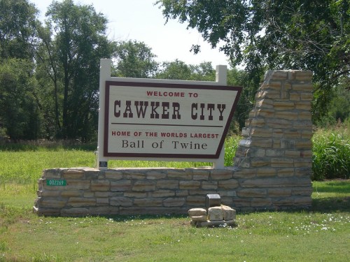 Welcome sign for Cawker City, home of the world's largest ball of twine, surrounded by greenery.