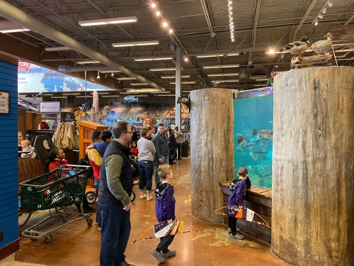 A busy store with a large fish tank, families browsing, and children fishing near the water.