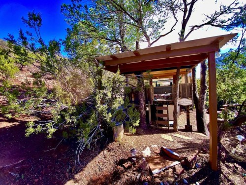 A rustic outdoor shelter surrounded by trees, with a wooden structure and scattered seating areas.