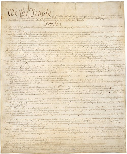 The image shows the U.S. Constitution, with "We the People" prominently at the top of the parchment.