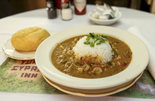 A bowl of gumbo with rice, served alongside a bread roll on a table with a placemat.