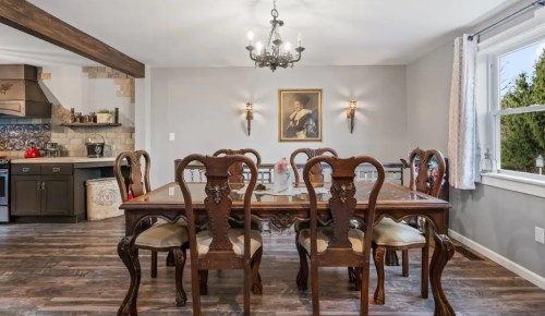 Elegant dining room with a large wooden table, ornate chairs, and a chandelier, featuring a portrait on the wall.