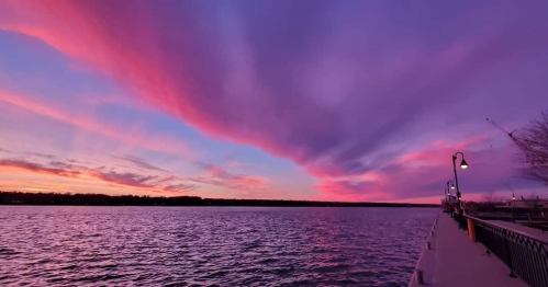 A serene waterfront scene at sunset, featuring vibrant pink and purple clouds reflecting over the water.