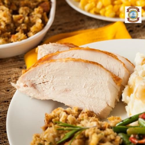 Sliced turkey breast on a plate with stuffing, mashed potatoes, and corn in the background.
