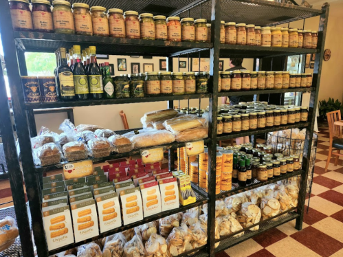A metal shelf filled with jars, oils, and various baked goods, including bread and cookies, in a cozy store setting.
