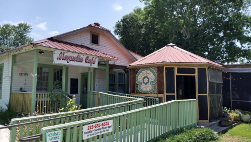 A charming café with a green porch and a decorative gazebo, surrounded by trees and a clear blue sky.