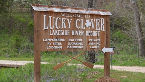 Wooden sign for Lucky Clover Lakeside River Resort, listing activities like camping, rafting, kayaking, and fishing.