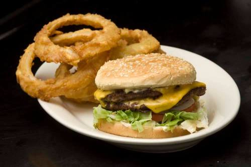 A cheeseburger with lettuce and tomato on a sesame seed bun, served with crispy onion rings on the side.