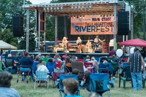 A band performs on stage at Riverfest, with an audience seated in lawn chairs enjoying the music.