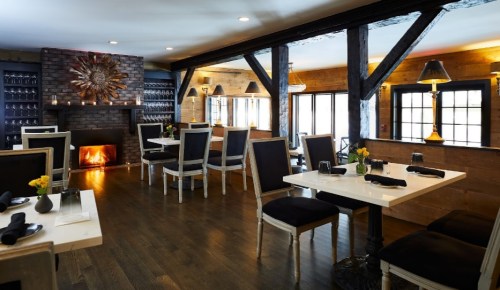 Cozy restaurant interior with wooden beams, tables set for dining, and a fireplace creating a warm atmosphere.
