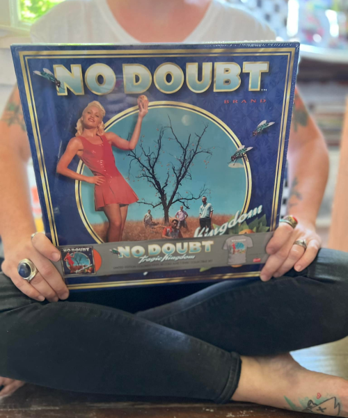 A person holds a No Doubt vinyl record cover featuring a woman in a red dress and a surreal landscape.