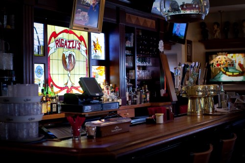 A cozy bar interior featuring a wooden counter, colorful stained glass, and a variety of liquor bottles on display.